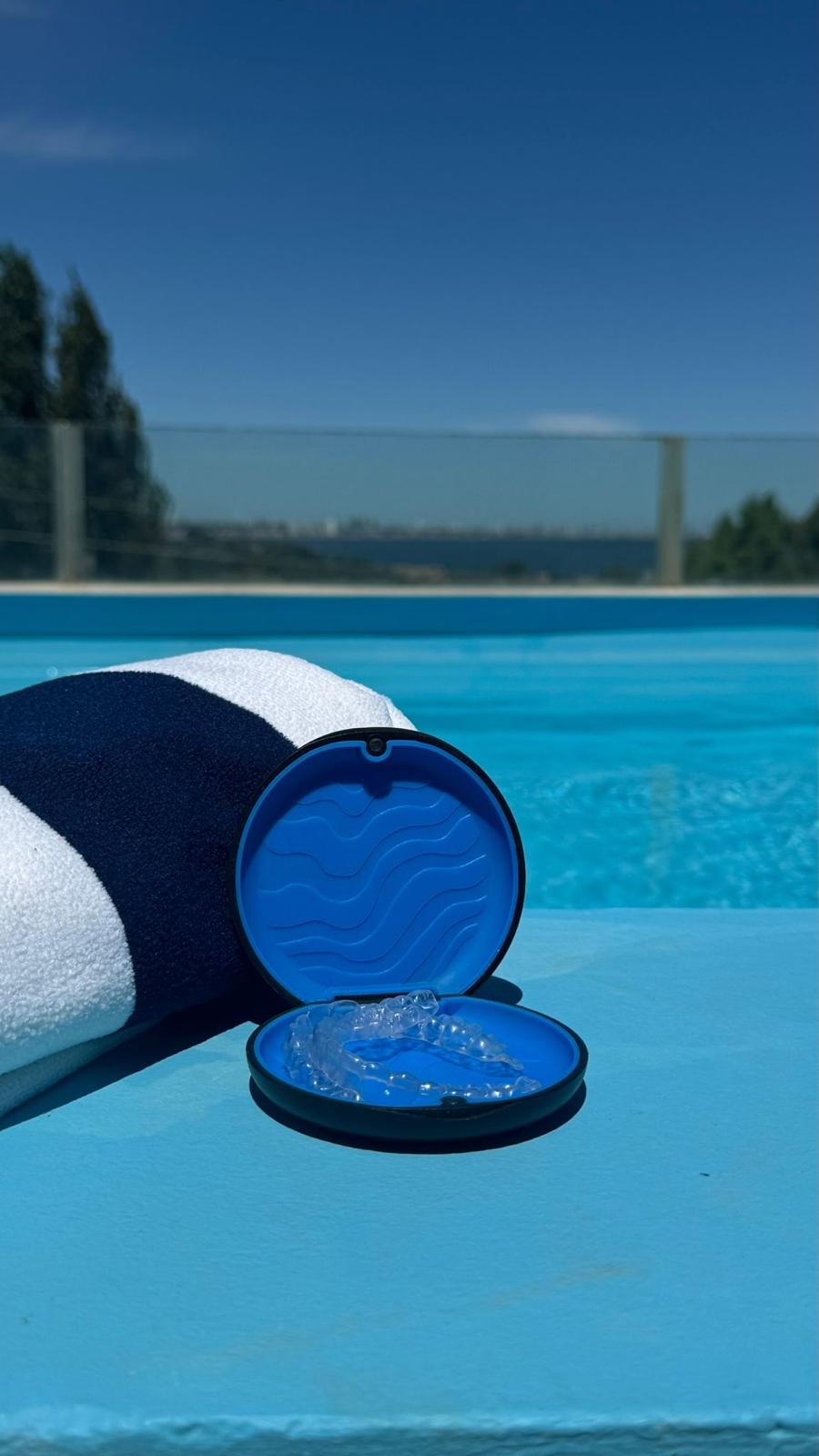 Estuche azul con alineadores apoyado junto a una toalla al borde de la piscina